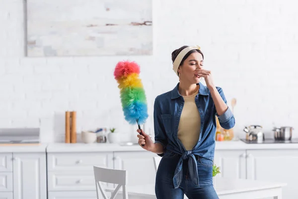 Ama de casa con cepillo de polvo estornudando en la cocina - foto de stock