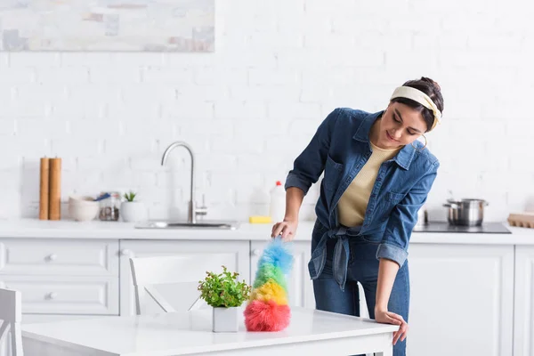 Mujer joven en camisa vaquera mesa de limpieza con cepillo de polvo - foto de stock