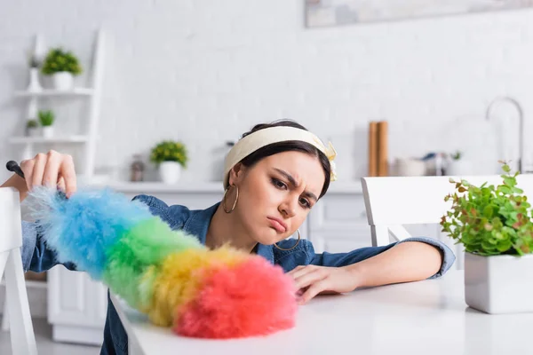 Triste tavolo pulizia casalinga con spazzola antipolvere vicino alla pianta offuscata — Foto stock