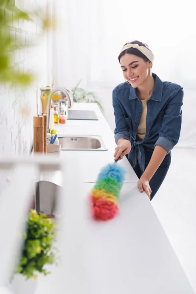 Fröhliche Hausfrau putzt Küchenarbeitsplatte mit Staubbürste — Stockfoto