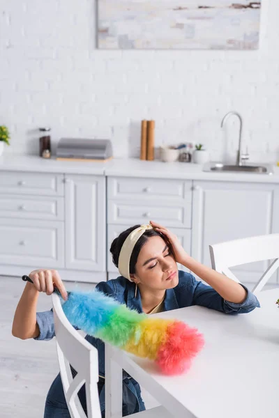 Femme au foyer fatiguée tenant brosse à poussière près de la table dans la cuisine — Photo de stock