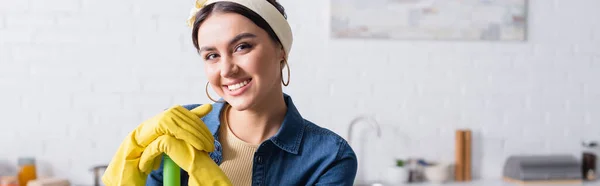 Sorrindo dona de casa em luvas de borracha segurando esfregona na cozinha, banner — Fotografia de Stock