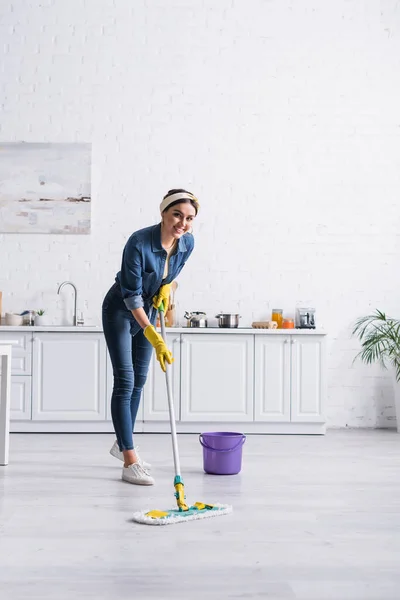 Happy housewife cleaning floor with mop in kitchen — Stock Photo