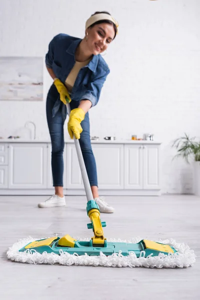 Fregona en el suelo en manos de una mujer sonriente sobre un fondo borroso en la cocina - foto de stock