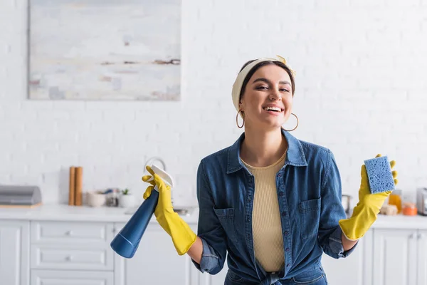 Femme au foyer souriante en gants de caoutchouc tenant éponge et détergent — Photo de stock