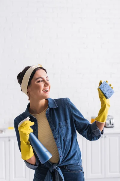 Fröhliche Hausfrau mit Schwamm und Sprühflasche in Küche — Stockfoto