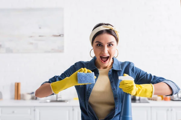 Femme au foyer excitée avec détergent pulvérisateur et éponge dans la cuisine — Photo de stock