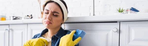 Sad housewife holding sponge and detergent near kitchen worktop, banner — Stock Photo