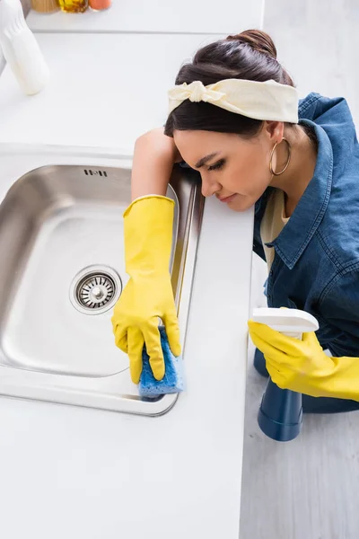 Hochwinkelaufnahme einer Frau in Gummihandschuhen, die Waschbecken mit Waschmittel und Schwamm wäscht — Stockfoto