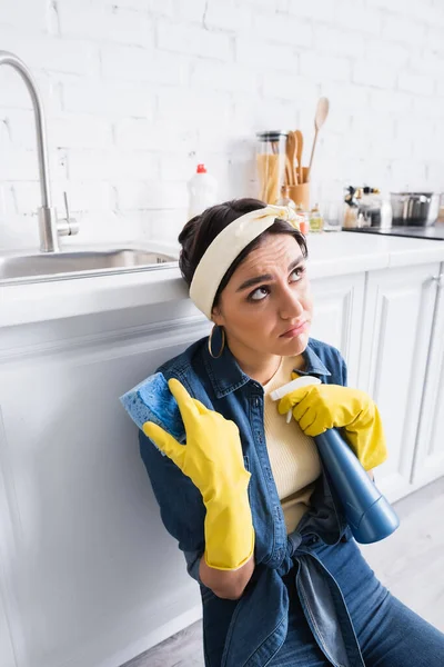 Femme au foyer pensive avec éponge et détergent près du plan de travail de la cuisine — Photo de stock