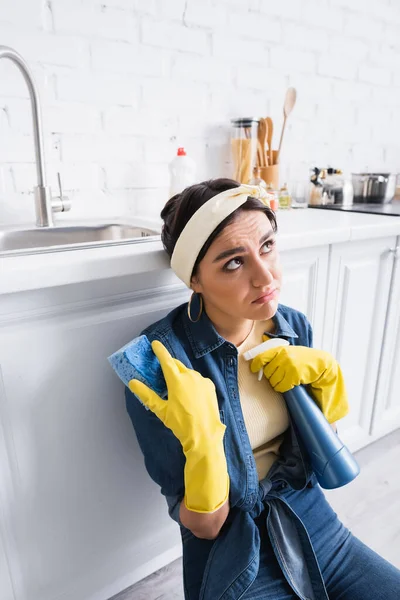 Ama de casa pensativa con esponja y detergente cerca de encimera de cocina - foto de stock