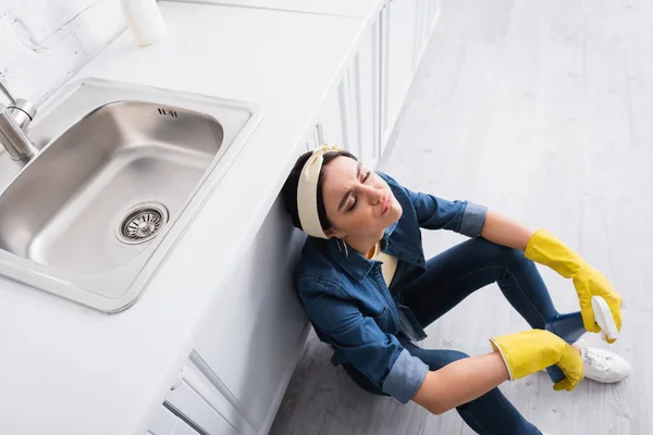 Overhead view of exhausted housewife with sponge and detergent sitting in kitchen — Stock Photo