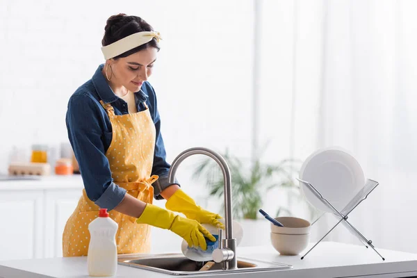 Junge Hausfrau wäscht Teller neben Spülmittel — Stockfoto