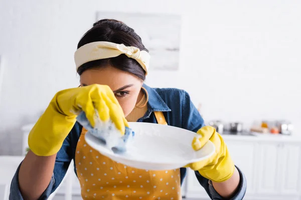 Домохозяйка держит губку и тарелку на размытом переднем плане — стоковое фото