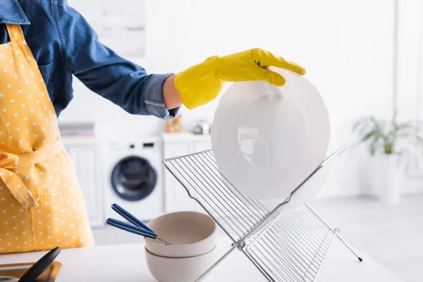 Vista recortada de la mujer en guante de goma placa de sujeción cerca de pie en la cocina - foto de stock