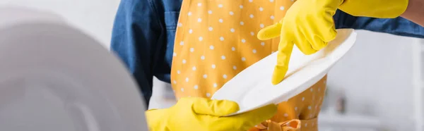 Cropped view of housewife in rubber gloves holding plate, banner — Stock Photo