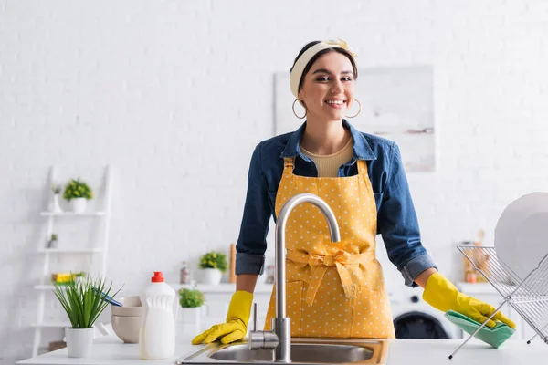 Mujer sonriente sosteniendo trapo cerca de platos y fregadero en la cocina - foto de stock