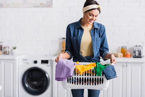 Sorrindo dona de casa olhando para roupas em cesta na cozinha — Fotografia de Stock
