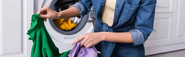 Vista cortada da mulher segurando roupas sujas perto de máquina de lavar roupa borrada, banner — Fotografia de Stock