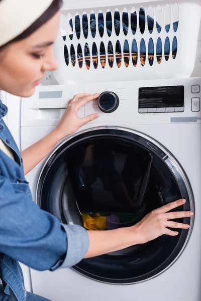 Casalinga offuscata che cambia lavatrice vicino al cestino con vestiti — Foto stock