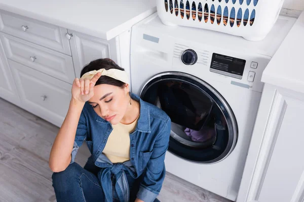 Вид зверху на виснажену домогосподарку, що сидить біля пральної машинки на кухні — Stock Photo