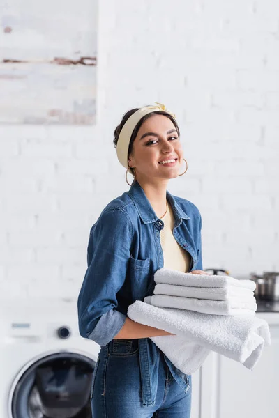 Junge Frau lächelt, während sie saubere Handtücher in der Küche hält — Stockfoto