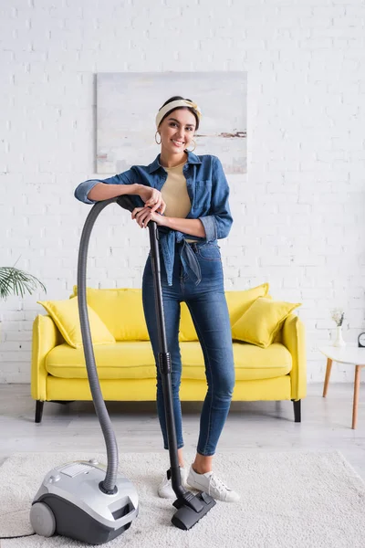 Femme au foyer souriante debout près de l'aspirateur à la maison — Photo de stock