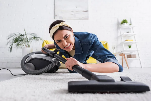 Angry woman cleaning carpet with blurred vacuum cleaner in living room — Stock Photo