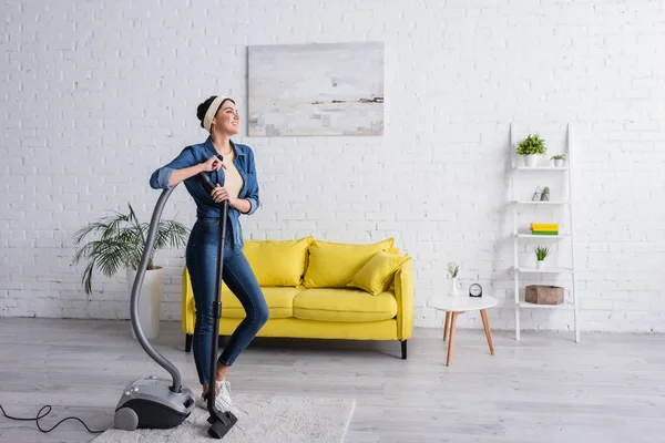 Happy housewife standing near vacuum cleaner at home — Stock Photo