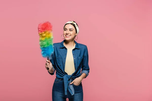 Sonriente ama de casa mirando cepillo de polvo aislado en rosa - foto de stock