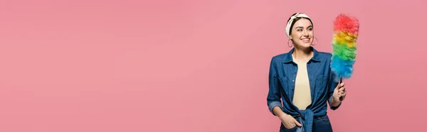 Cheerful housewife looking at dust brush isolated on pink, banner — Stock Photo