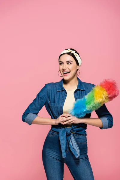 Positive Hausfrau im Stirnband hält Staubbürste isoliert auf rosa — Stockfoto