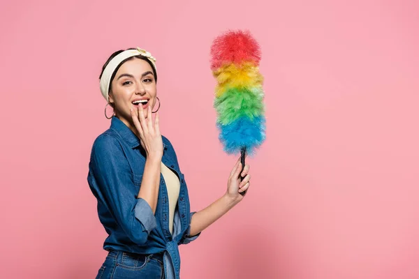 Aufgeregte Frau im Jeanshemd mit Staubbürste auf rosa Hintergrund — Stockfoto