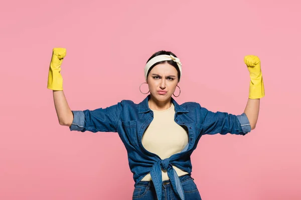 Junge Hausfrau in Gummihandschuhen zeigt Muskeln isoliert auf rosa — Stockfoto