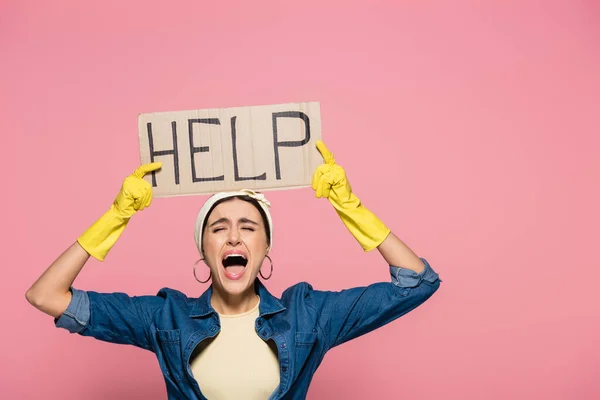 Screaming housewife in rubber gloves holding placard with help lettering isolated on pink — Stock Photo