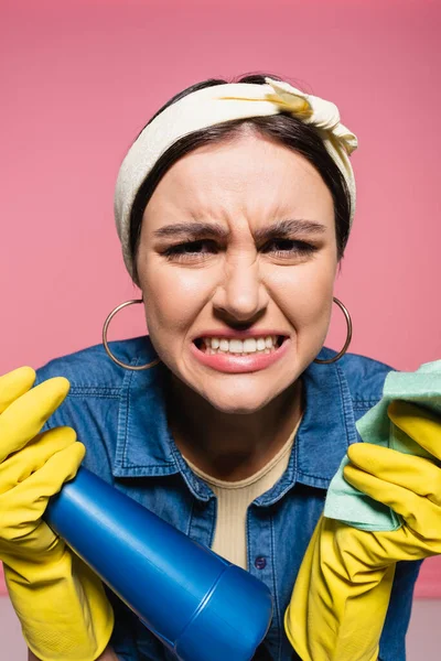 Wütende Hausfrau mit Waschmittel und Lappen blickt isoliert auf rosa Kamera — Stockfoto