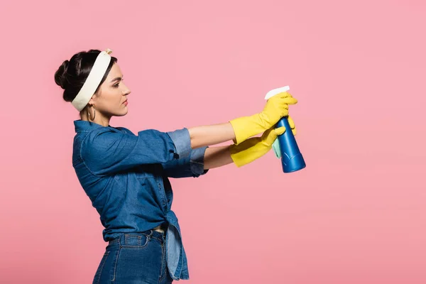 Vista lateral da dona de casa segurando detergente e pano isolado em rosa — Fotografia de Stock
