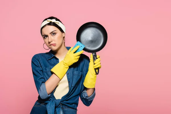 Housewife with sponge and frying pan biting lips isolated on pink — Stock Photo
