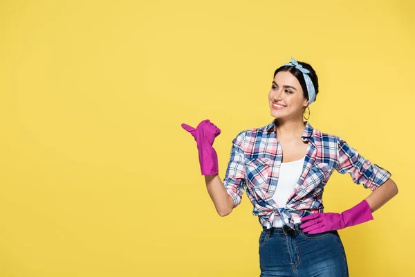 Smiling woman in rubber gloves pointing away isolated on yellow — Stock Photo