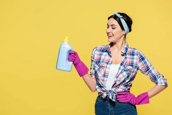 Smiling housewife holding bottle of detergent isolated on yellow — Stock Photo