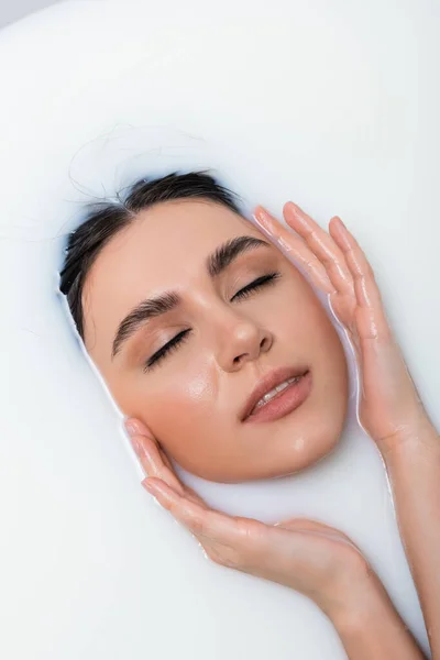 Sensual mujer tocando la cara mientras se relaja en el baño con leche - foto de stock