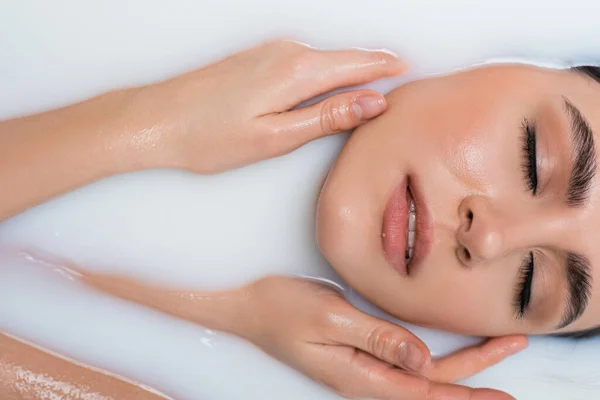 Sensual woman touching face while relaxing in milk bath — Stock Photo