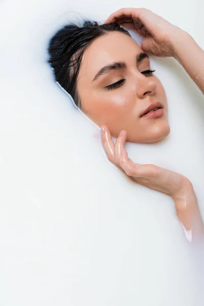 Bella giovane donna toccare il viso mentre si prende il bagno di latte — Foto stock