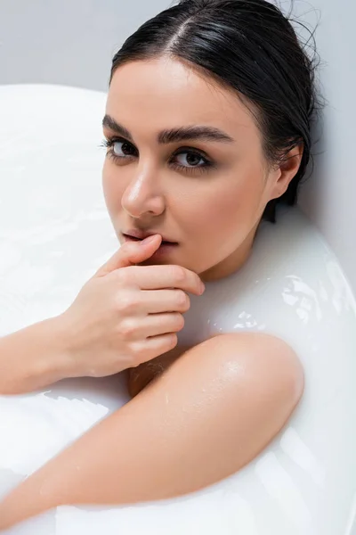 Seductive woman looking at camera and touching lip while taking bath with milk — Stock Photo