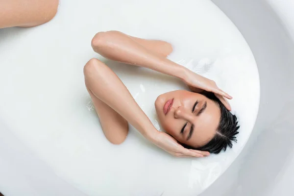 Mujer con los ojos cerrados tocando el pelo mientras toma el baño con leche - foto de stock