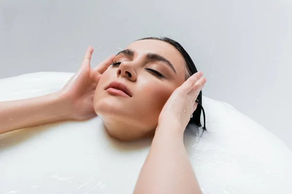 Sensual mujer tocando el pelo mojado mientras disfruta del baño de leche - foto de stock