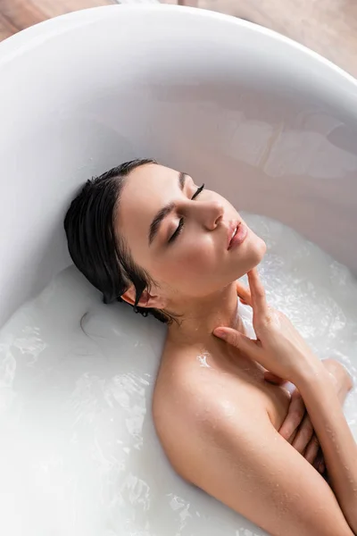 Seductive woman with closed eyes relaxing in bathtub with milk — Stock Photo