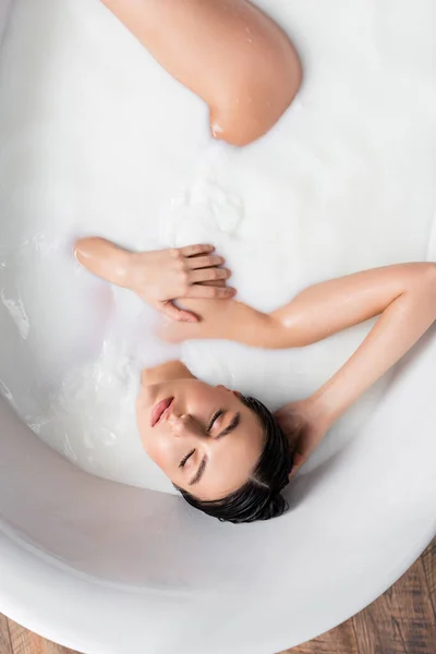 Vue de dessus de la femme sensuelle couvrant le sein tout en prenant un bain de lait — Photo de stock