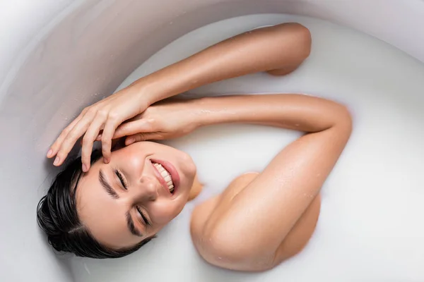 Young woman smiling with closed eyes while relaxing in bathtub with milk — Stock Photo