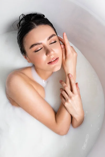 Overhead view of young woman touching face while bathing in milk — Stock Photo